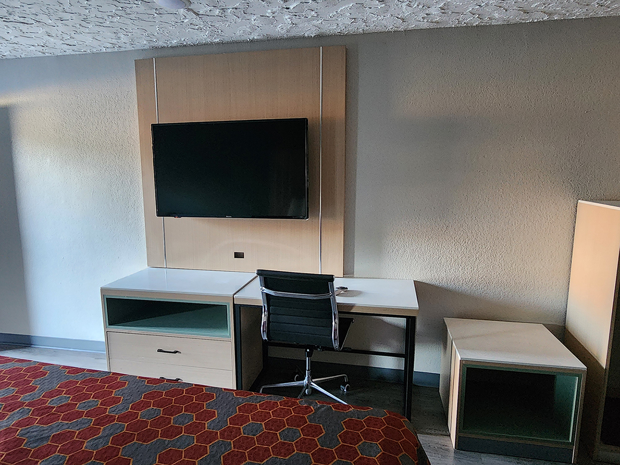 A king room at the Americas Best Value Inn Longview with a flat-screen TV on the wall over a desk area with a chair.