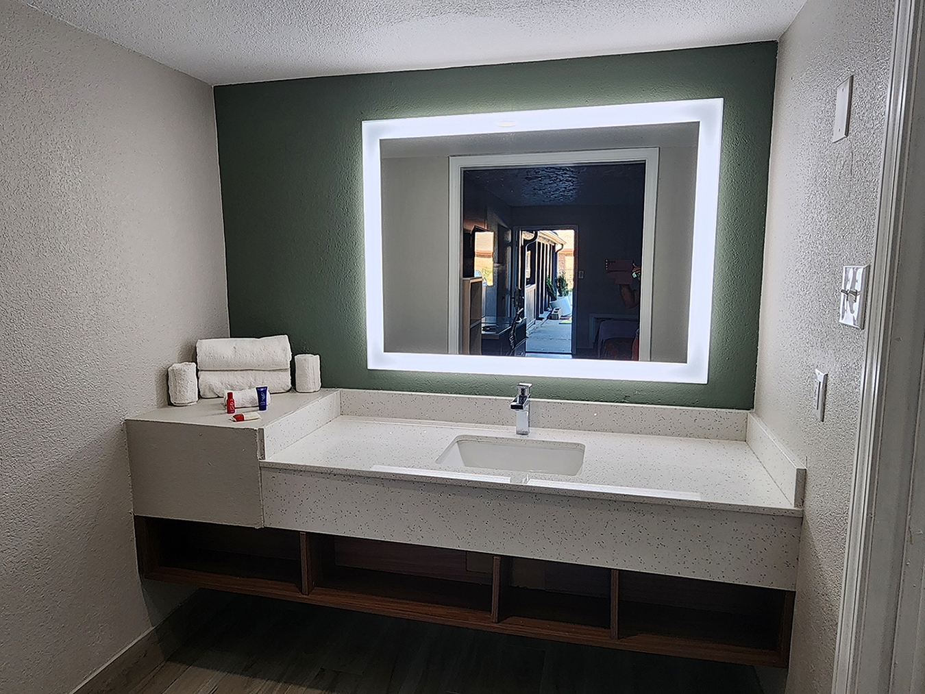 The vanity area in a king room at the Americas Best Value Inn Longview with a counter, sink, mirror outlined with lights, and towels stacked in the corner.