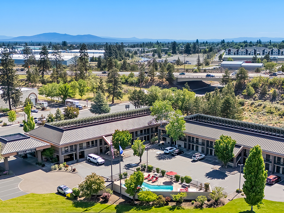 An aerial view of the pool, lawn area, parking lot, and exterior of the Red Lion Inn & Suites Deschutes River Bend hotel.
