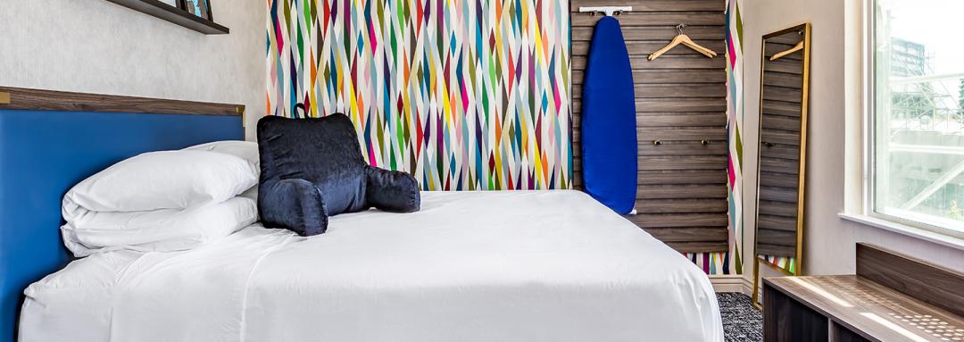 Guest room with queen bed, ironing board, and artistically designed wall