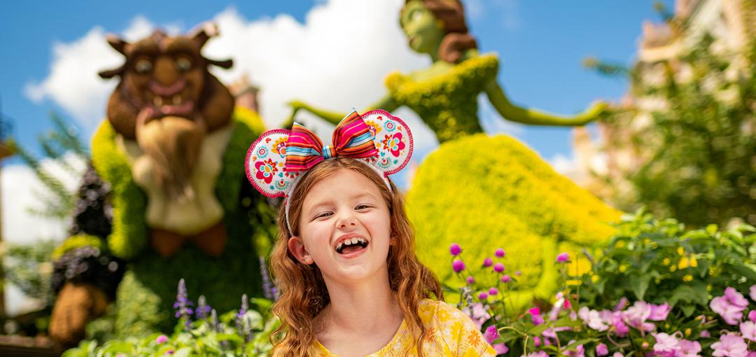 a smiling child standing in front of Disney Character topiaries at the EPCOT® International Flower & Garden Festival