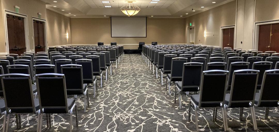 Conference room setup with rows of chairs facing a screen and podium.