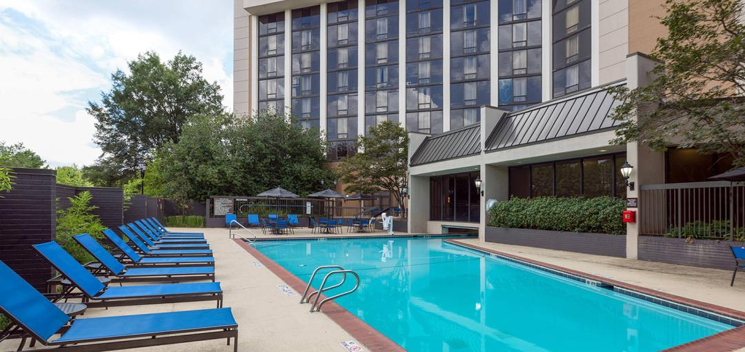 Outdoor swimming pool area at Sonesta Atlanta Northwest Galleria with blue lounge chairs and tables with umbrellas.