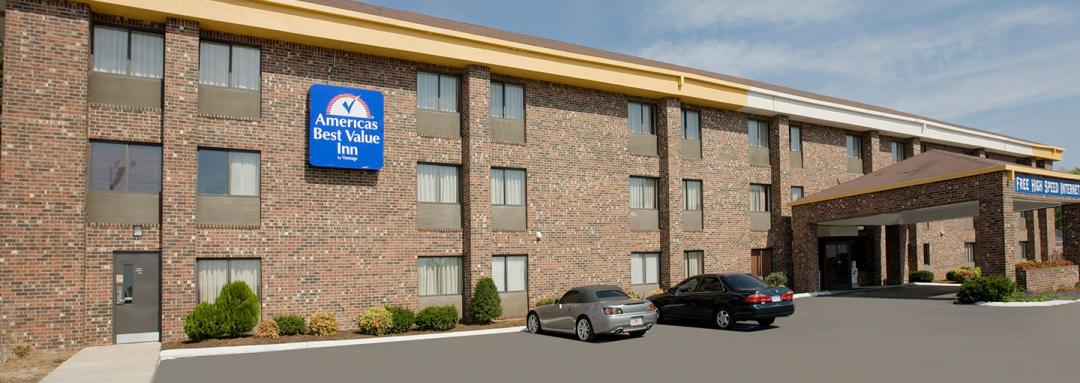 Hotel exterior with two cars in parking lot and blue Americas Best Value Inn sign