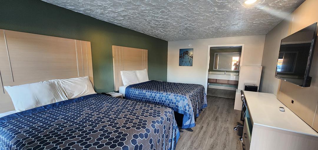 A two-queen room with blue bedspreads, a flat-screen tv on the wall, and a bathroom vanity at the Americas Best Value Inn Longview hotel.