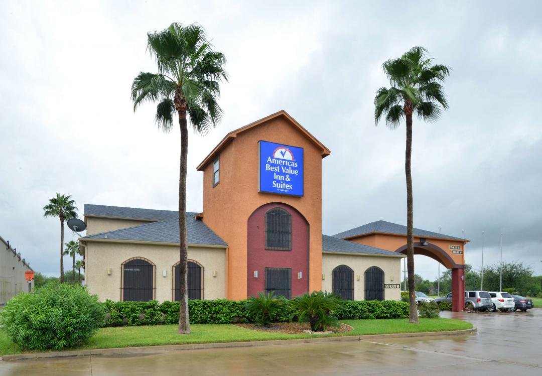 Hotel lobby exterior with lawn area and palm trees on rainy day