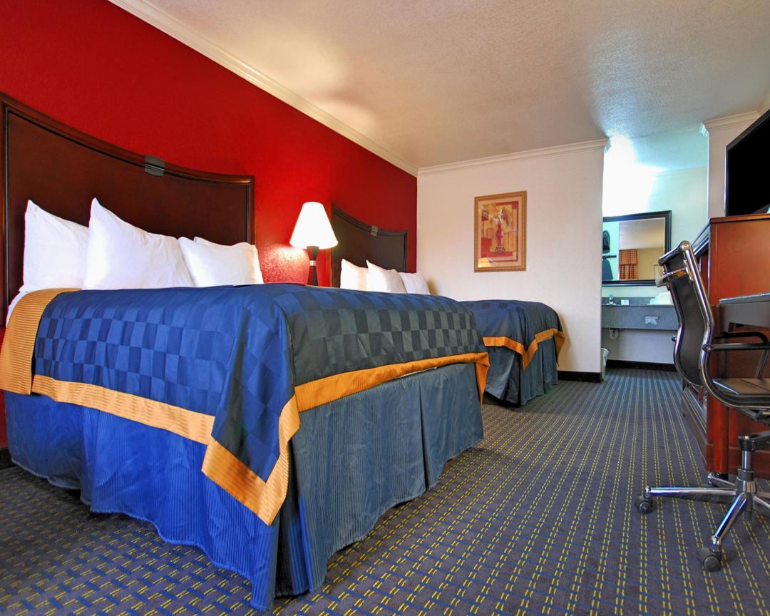 Two Queen Beds, blue and orange sheets, red wall, chair with desk
