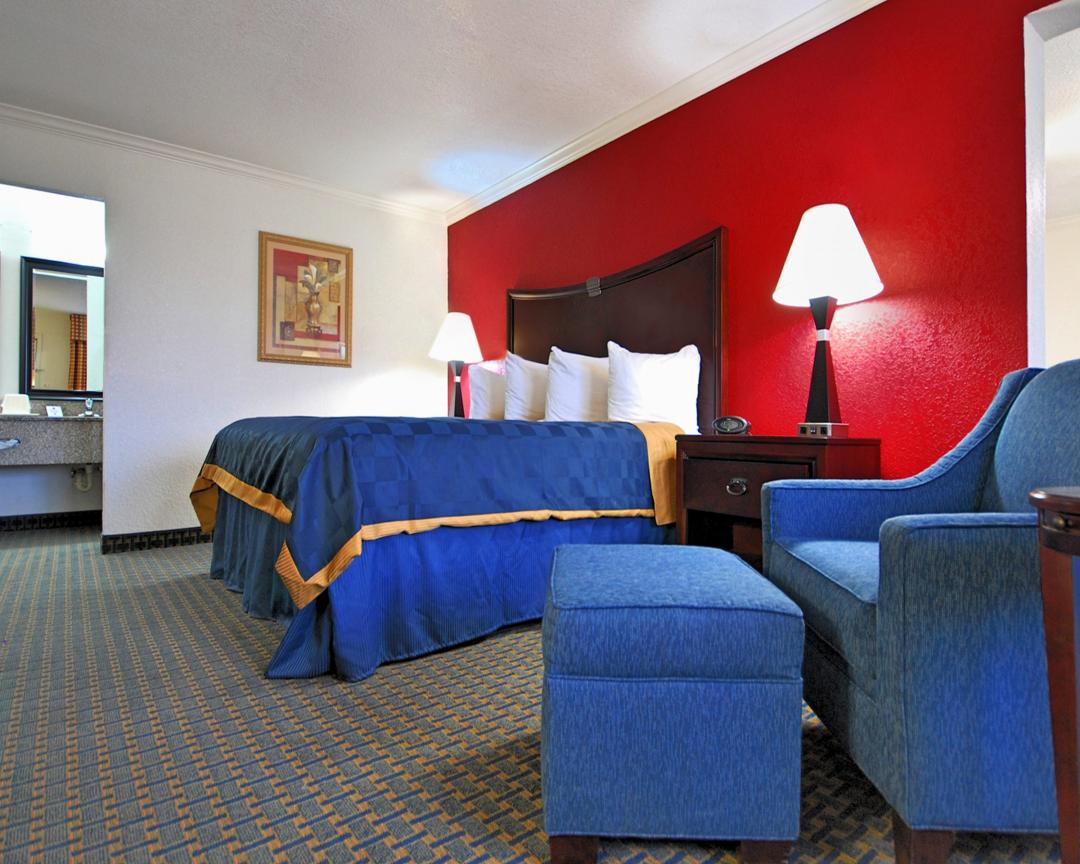 One King Bed, red wall, blue and orange sheets, white pillows, blue chair